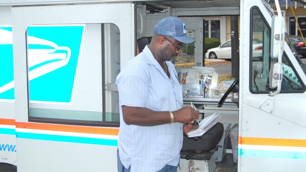 Postal service worker looking at mail infront of a mail truck.